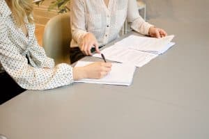 woman writing on notepad next to woman another woman reading documents